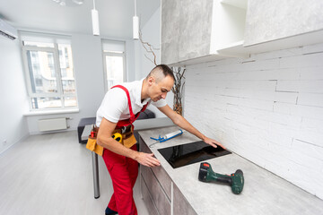 Fototapeta na wymiar Young Repairman Installing Induction Cooker In Kitchen