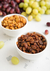 Bowls of green and red dark raisins with ripe raw grapes on light background.Macro.