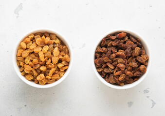 Two bowls with sweet dried green and brown raisins on light background.Top view.