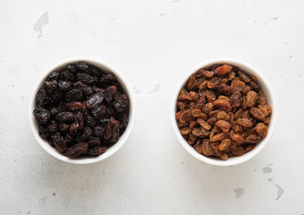Two bowls with sweet dried brown and dark raisins on light background.Top view.
