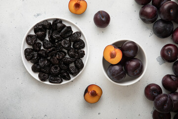 Dried prunes and ripe raw plums on light background.Top view.