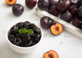 Dried sweet prunes with ripe plums in wooden box on light kitchen background.