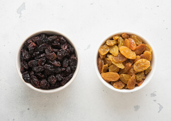 Two bowls with sweet dried green and dark raisins on light background.Top view.