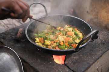 Indian village woman cooking mixed vegetables in a frypan.