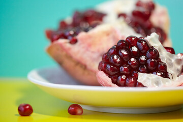 Close up of raw red ripe pomegranate with sliced pomegranate on white plate.