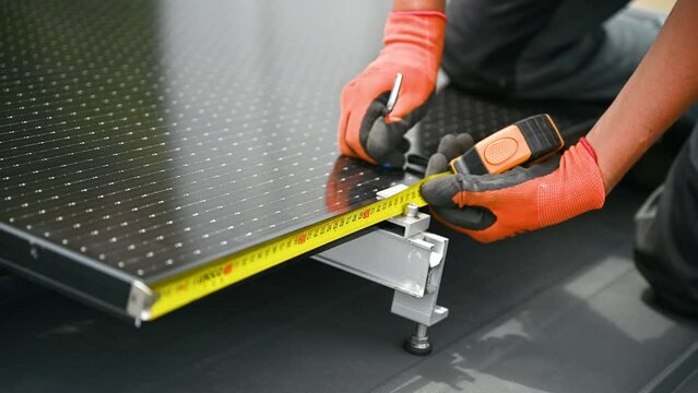Worker building solar panel system on rooftop of house for generating electricity through photovoltaic effect. Close up man using ruler to measure mounting equipment for precise installation.
