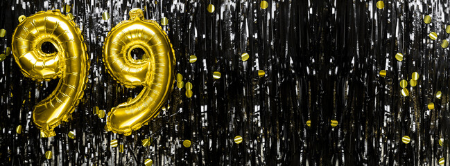Gold foil balloon number number 99 on a background of black tinsel decoration. Birthday greeting...