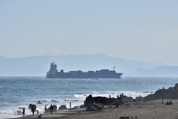 海峡を渡るタンカーと浜で遊ぶ観光客