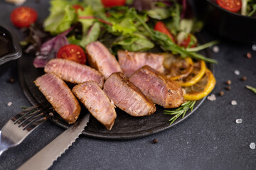 sliced grilled Organic Tuna Steak on black ceramic serving dish with salad on a table