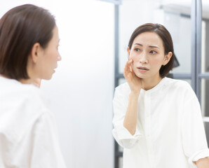 Obraz premium 鏡にうつる自分の肌を見ているミドル世代の女性