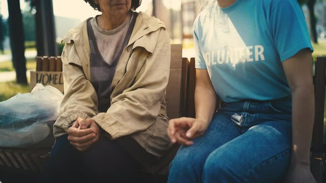Female volunteer talking with poor homeless senior woman, social assistance