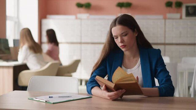 Woman turns page of book sitting at desk