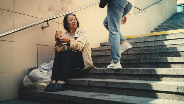 Angry woman showing aggression to homeless old female asking for help on stairs