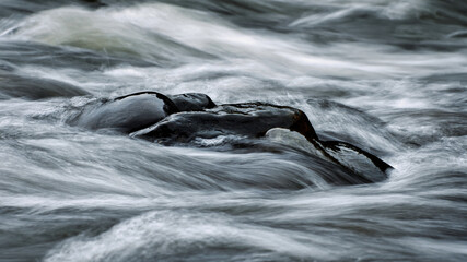 Schwarzer Stein im fließendem Wasser. Strömung umspühlt Steine. Fluß fließt um einen...