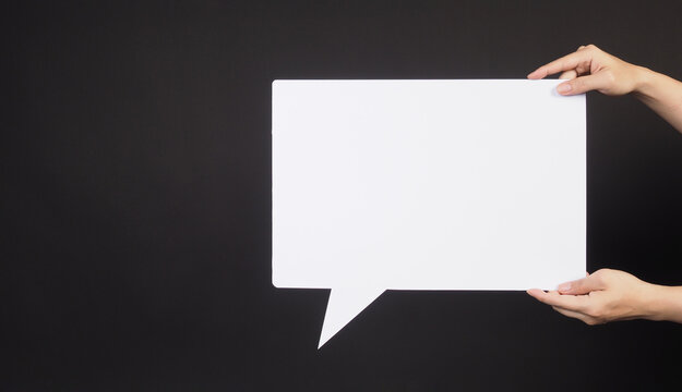 Hand is holding blank speech bubble on black background.