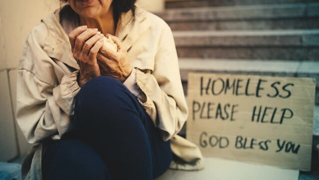 Lonely senior homeless woman eating bread hungrily, begging on stairs, poverty