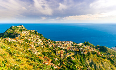 Obraz premium scenic view from highland to a mountain town with beautiful buildings, castles, hills and slopes and panoramic sea gulf with cloudy sky on background