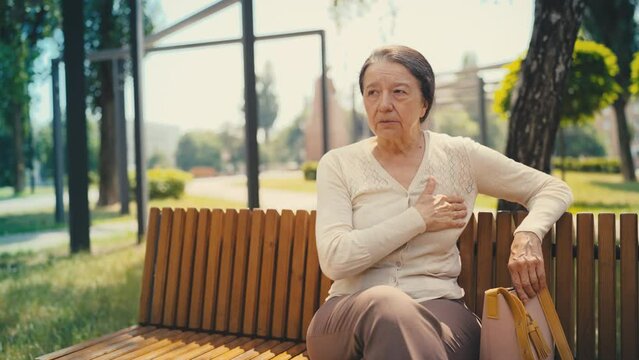 Senior woman suffering acute pain in chest while sitting on bench, heart failure