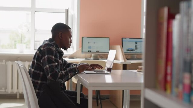 Man works with laptop in computer class. Black guy immersed in internet surfing uses college laptop equipment for seeking. Preparation with technology