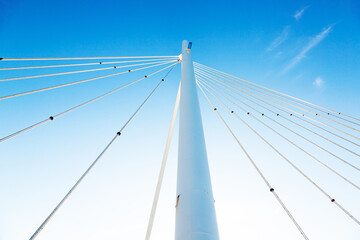 White vertical pillar of a bridge with steel braces, against a background of blue sky, view from below. - obrazy, fototapety, plakaty