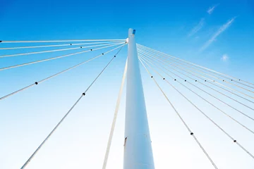 Foto op Aluminium White vertical pillar of a bridge with steel braces, against a background of blue sky, view from below. © Сергей Жмурчак
