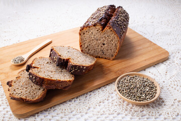 Sliced dark rye hemp seed bread on wooden board on linen towel. Healthy pastry