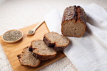 Sliced dark rye hemp seed bread on wooden board on linen towel. Healthy pastry