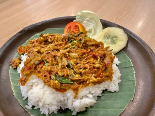 close up traditional Indonesian shreded duck chicken  ayam geprek with hot spicy chili sauce sambal on stone wooden green leaf plate steamed rice and raw vegetables as side dish