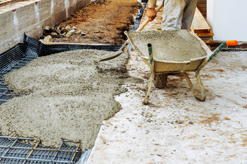 Worker in protect gloves is unloads the concrete by shovel from building trolley  in construction site. Concept of using of construction materials during construction