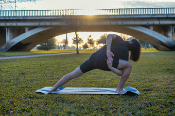 Young Man With Athletic Body Practicing Yoga At Sunset In A City Park.
