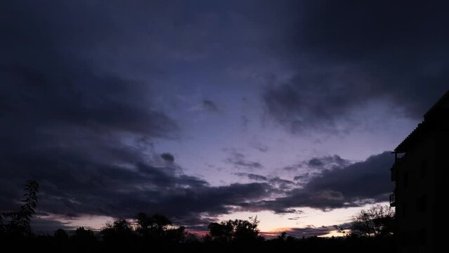 Last pink rays of the sun above the Great Hungarian Plain on a windy evening. Magnificent nature landscape, dark clouds moving against the blue sky. Fast motion sunset with beautiful lights.