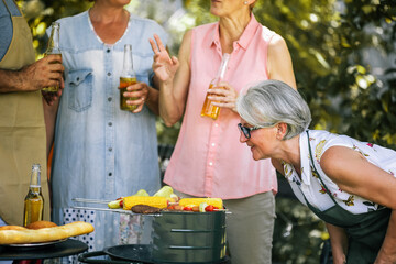 Elderly people are making barbeque, drinking beverages, making memories, and laughing.