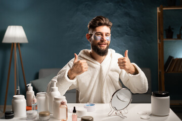 Handsome bearded man wears bathrobe recommended collagen patches under eyes, looking at camera doing daily evening beauty routine. beauty, skin care and people