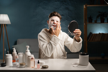 Bearded man applying moisturizing sheet mask for face doing daily evening skin care