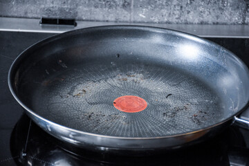 Large dirty Teflon pan in black and silver color for cooking and frying. On the black induction stove in the kitchen