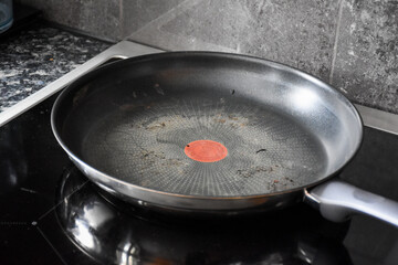 Large dirty Teflon pan in black and silver color for cooking and frying. On the black induction stove in the kitchen