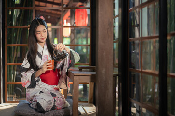 Pretty the Traveller Young Asian woman wearing a Japanese traditional kimono dress, a Yukata dress, and holding an umbrella is happy and cheerful in the green natural park.
