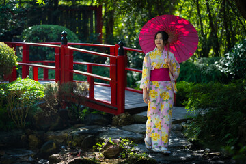 Pretty the Traveller Young Asian woman wearing a Japanese traditional kimono dress, a Yukata dress, and holding an umbrella is happy and cheerful in the green natural park.