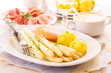 Traditional German white asparagus with boiled potatoes  and ham served as close-up on a design plate