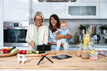 Three Generations Family. Grandma, mother and baby record a cooking vlog or podcast while chopping vegetables for a healthy vegetarian meal in the kitchen and stream it online. Vegan food preparation