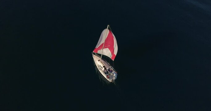 Yacht sailing on open sea with red sails aerial view. Nature seascape with sail boat cruising at ocean bay. Cinematic summer vacation scenery