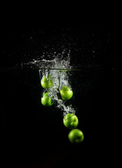 Green plum dropped into water with bubbles isolated on a black background.
