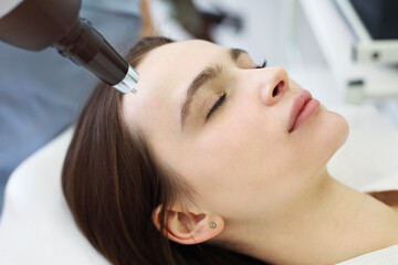 Woman treating client face with laser