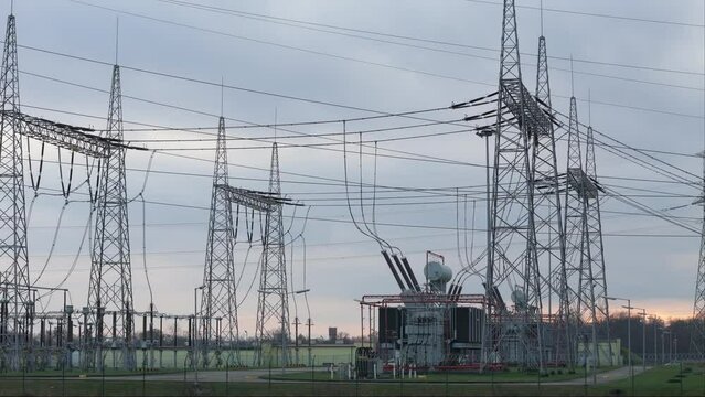 A transformer station is highlighted against a backdrop of sunset clouds in drone and ground-level footage. The intricate interplay of high-voltage poles, lattice structures, cables, and transformers