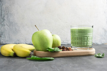 Green detox smoothie in a glass, blended vegetarian drink from spinach leaves, apple, banana fruit...