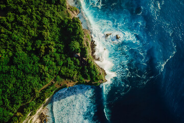 Aerial down view of coastline with rocky cliffs, sea with waves and lighthouse in Bali