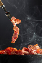 Fried steaming bacon slices on a black background.