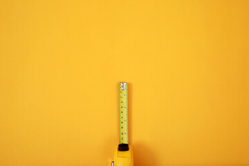 The yellow measuring tape for the mason is placed on a yellow background. Soft focus.