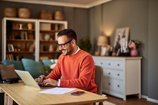 A happy adult freelance working on his laptop and writing an email to a client.