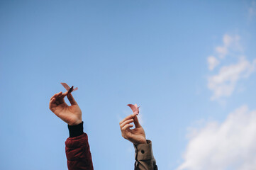 Two female hands hold paper cranes against the background of a blue sky with clouds. Origami, bird....